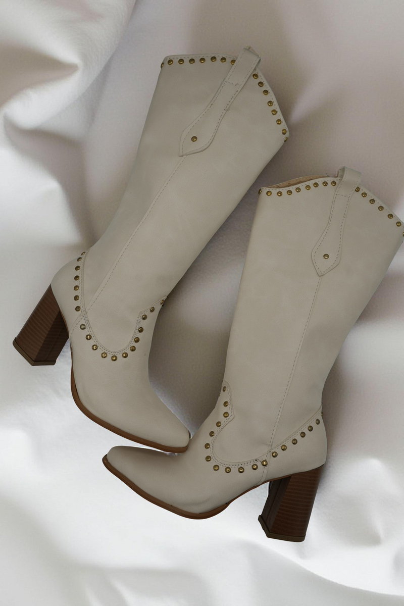 Pair of beige cowboy boots with brown soles on a white fabric background